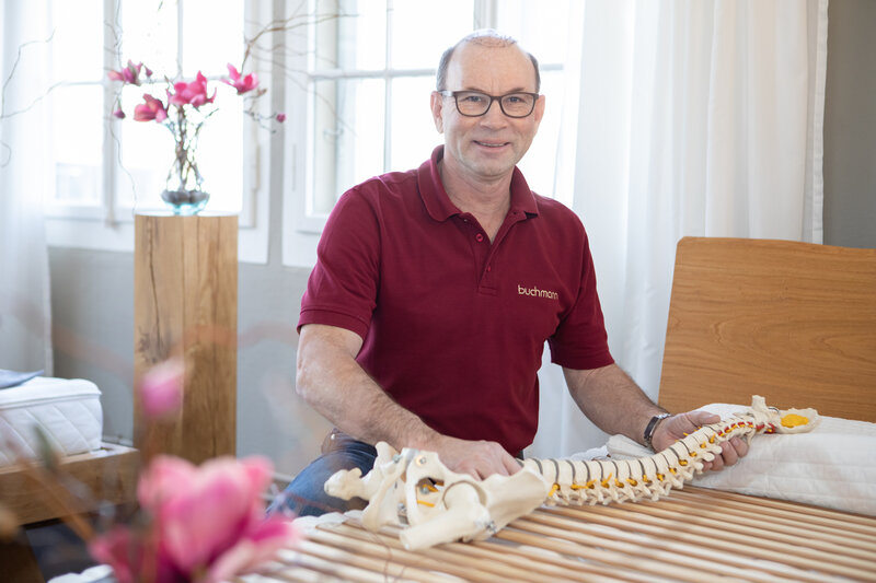 Schlafberater Erwin Buchmann mit Rückenskelett auf Bettrost | © Buchmann Schreinerei AG